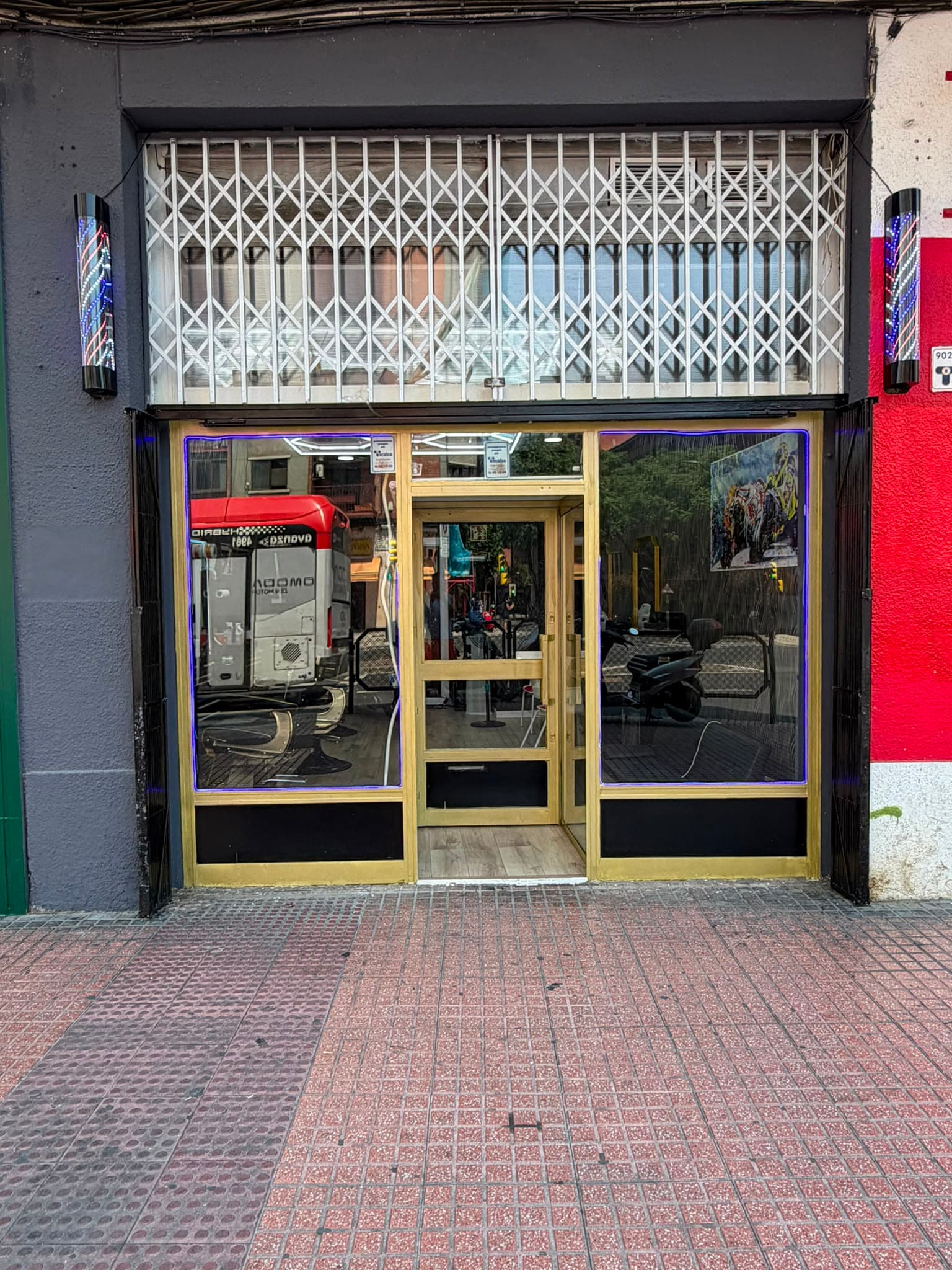 Fachada de El Maestro en Duquesa Villahermosa 7: escaparate con marco dorado entre dos postes de barbero iluminados.